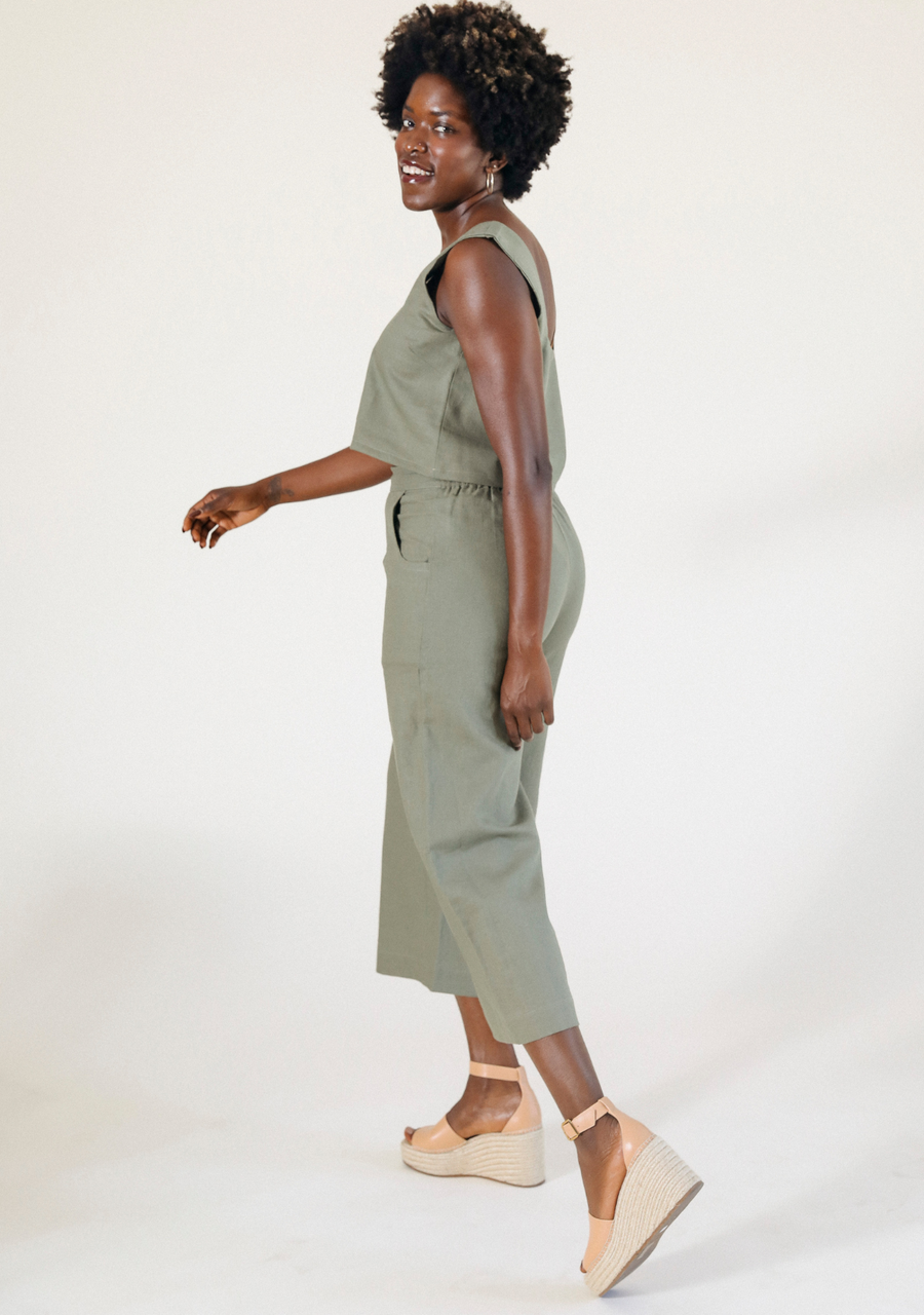 Side profile of a model walking while wearing the olive green Poplinen Nin Linen Pant paired with beige espadrille wedges.