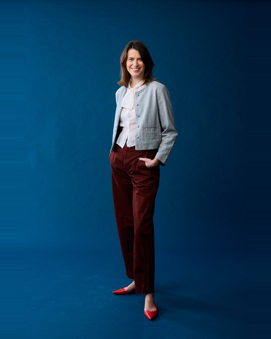 Viva Voce CEO Amy wearing the Reistor Lady Jacket in Grey Cotton Tweed against a blue backdrop.