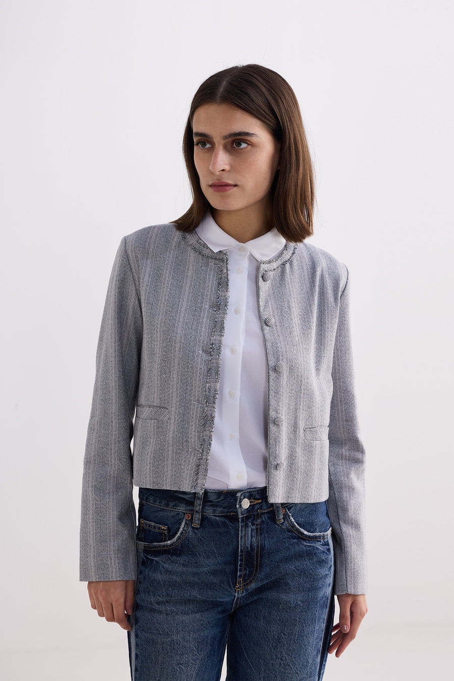 Front view of model wearing the Reistor Lady Jacket in Grey Cotton Tweed over a white collared shirt and blue jeans.