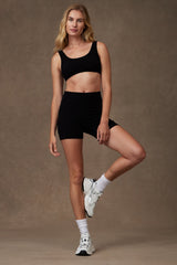 Studio model wearing the black Reprise Activewear Sage Pocket Shorts in 5-inch inseam paired with a matching black sports bra