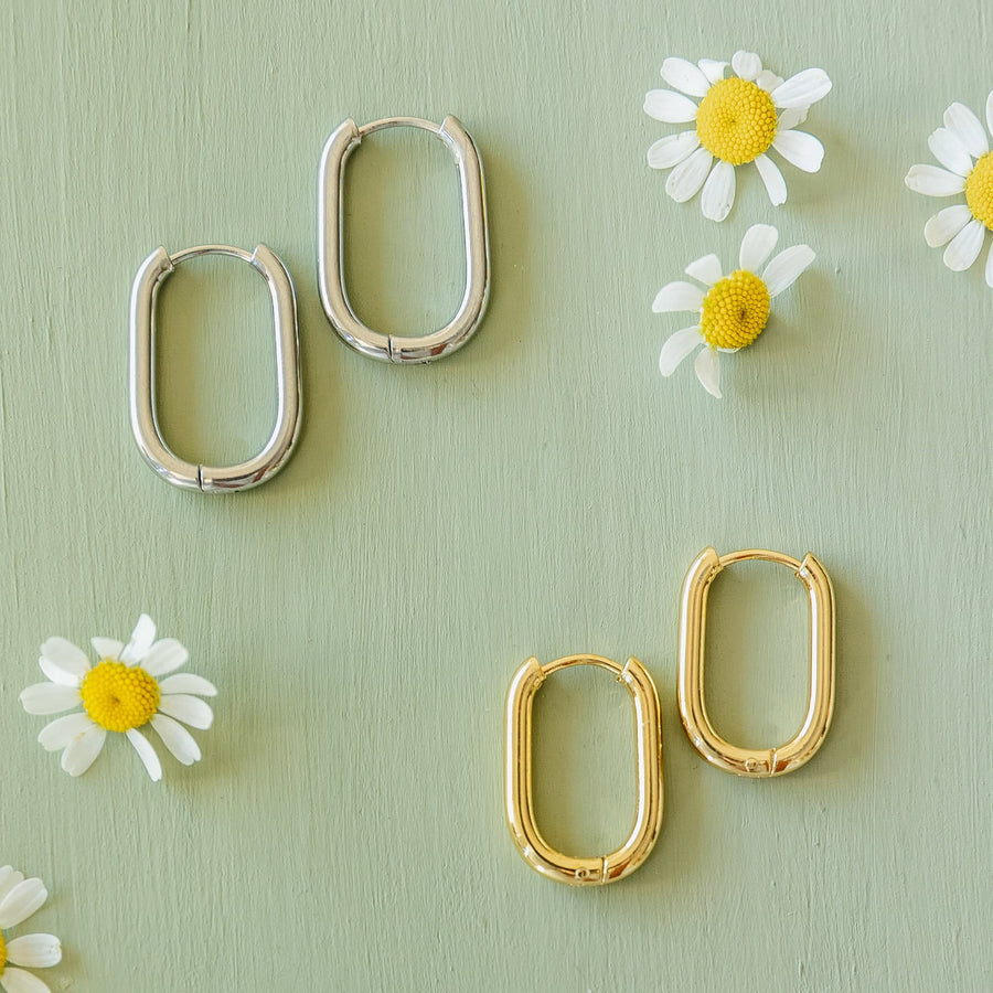 Both gold and silver variants of the Sela Designs Rectangle Everyday Hoop Earrings displayed on a sage green background with white daisy blossoms.