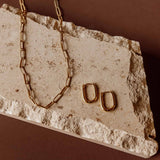 Gold Sela Designs Rectangle Everyday Hoop Earrings paired with a matching gold paperclip link chain on a stone slab.