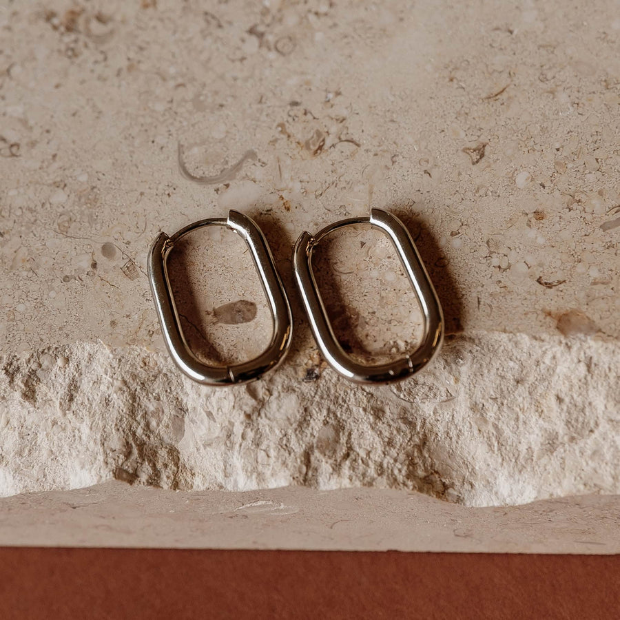 Pair of tarnish-free silver-plated Sela Designs Rectangle Everyday Hoop Earrings displayed on stone.