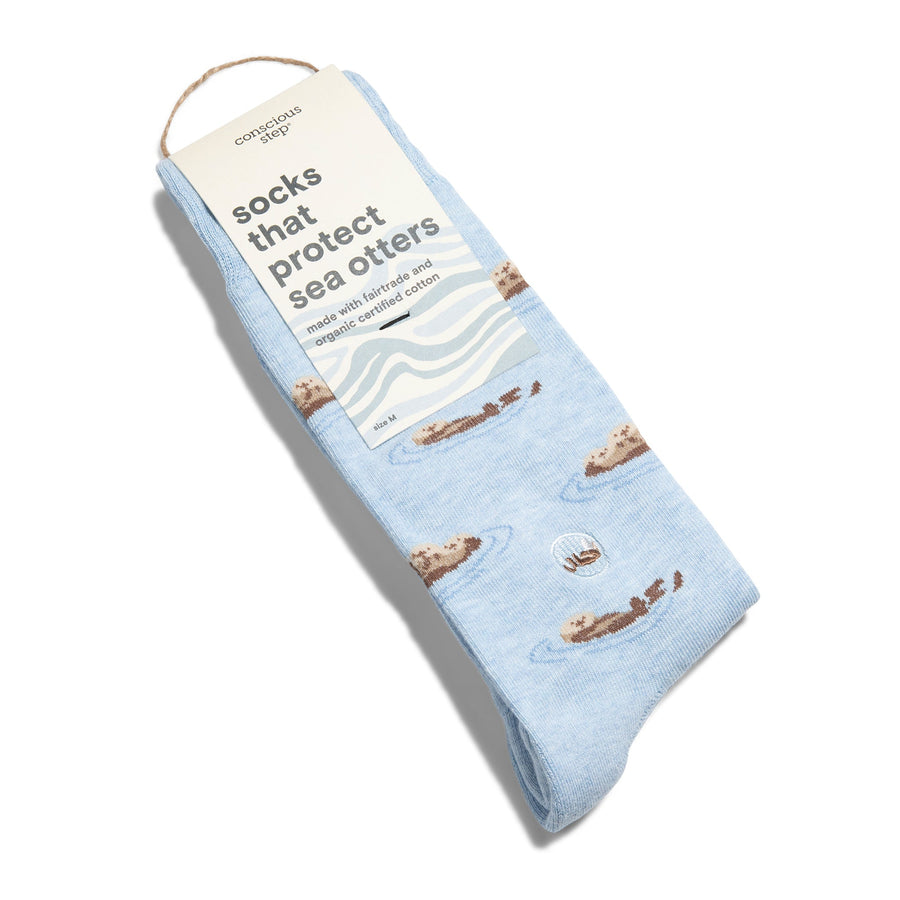 A single pair of light blue Conscious Step sea otter socks folded flat with a cream card stock packaging sleeve that reads "socks that protect sea otters made with fairtrade and organic certified cotton".