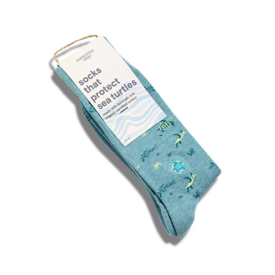 A single pair of light teal Conscious Step sea turtle socks folded flat with a cream card stock packaging sleeve that reads "socks that protect sea turtles made with fairtrade and organic certified cotton".