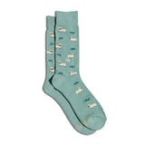 Studio flat lay portrait of a pair of sage green Conscious Step Socks That Save Sheep showcasing the sheep pattern and embroidered sheep emblem.