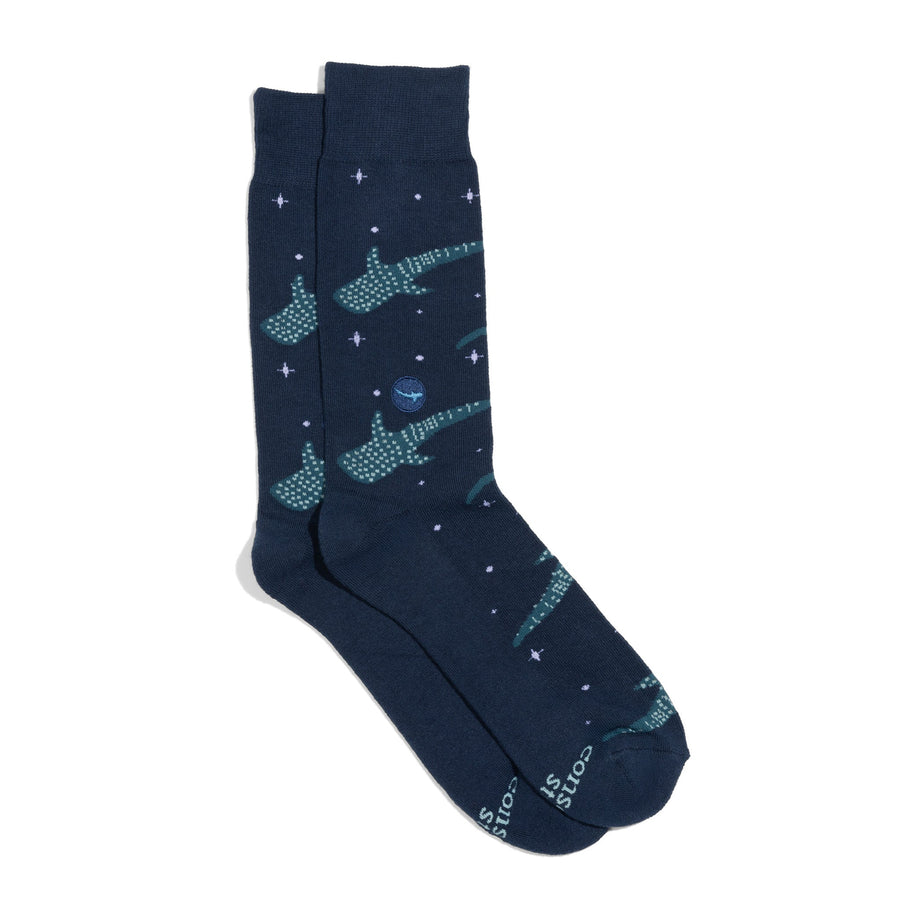 A pair of dark navy blue crew socks from Conscious Step featuring a green whale shark pattern with small white and purple starburst dots, and a circular embroidered shark patch on the ankle, shot on a white background.