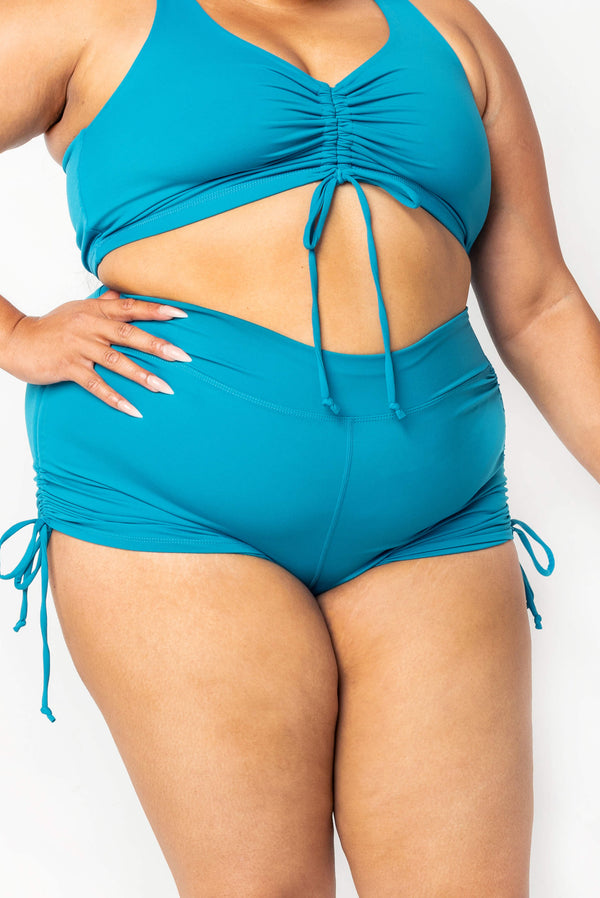 Front view close-up of a plus-size model wearing high-waisted teal Superfit Hero swim booty shorts paired with a matching cinched bikini top.