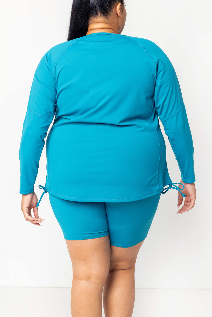 Back view of a model showing the full coverage and relaxed fit of the teal Superfit Hero long sleeve rash guard.