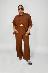 Full-length studio photo of a model wearing the Baacal Payton shirt jacket and matching Riley wide-leg pants set in terracotta styled with blue sneakers.