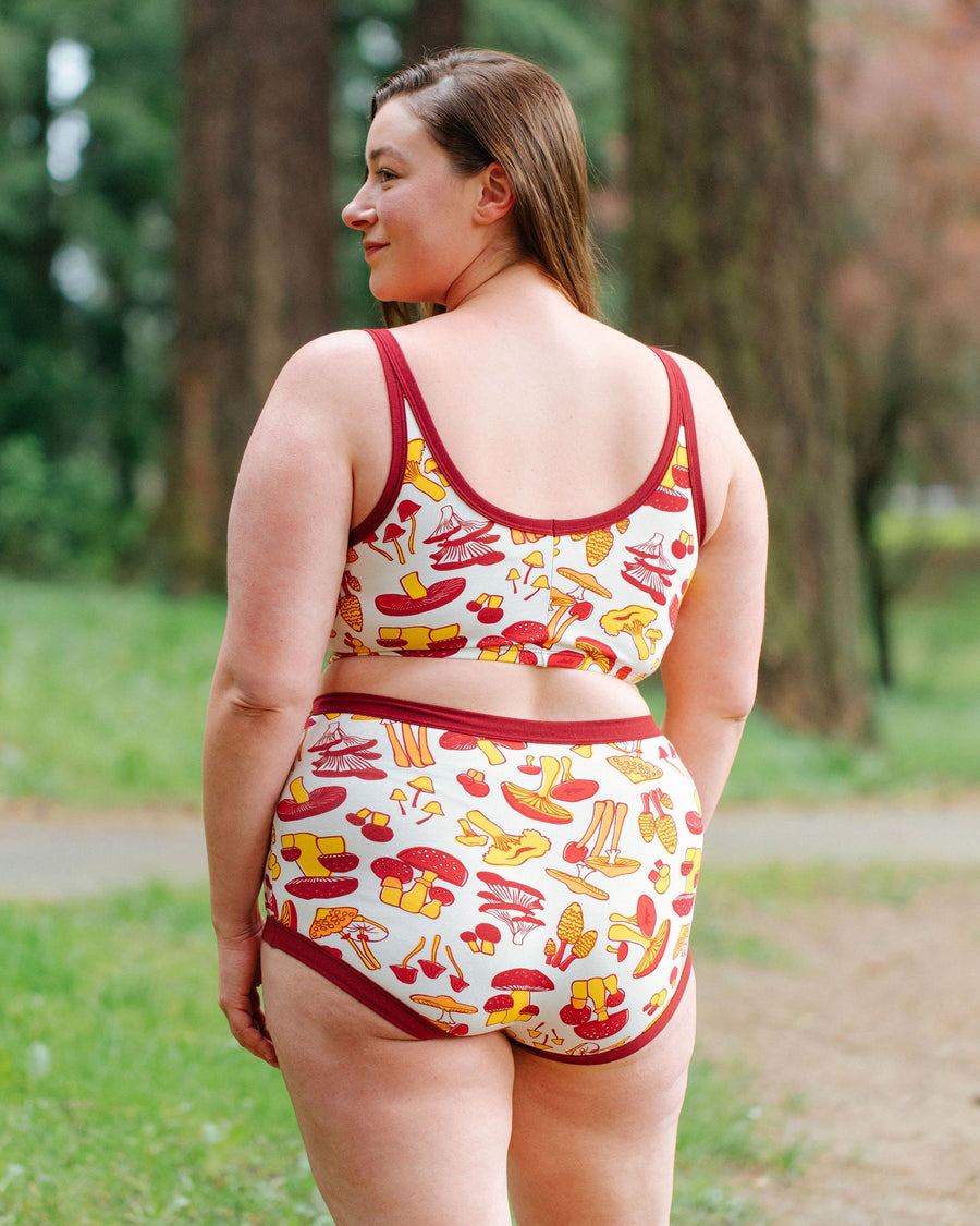 Side and back profile view of model Jennice wearing the organic cotton Thunderpants USA Longline Bra in mushroom print outdoors.