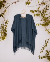 Dark charcoal navy Village Thrive Rayon Kimono hanging against a white wall framed by green foliage.