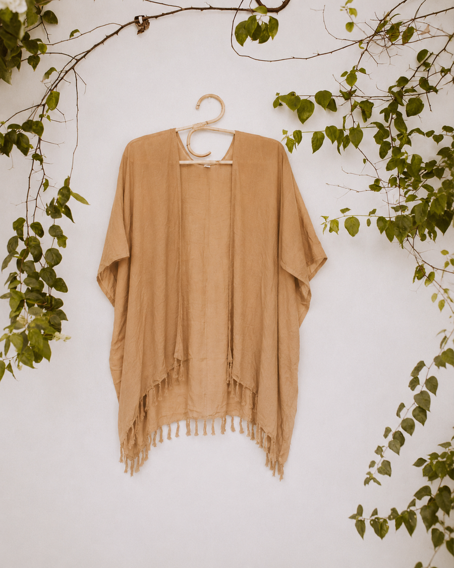 Desert Gold Village Thrive Solid Color Kimono with tassel hem hanging on a wooden hanger.