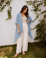 Model wearing the soft slate blue Village Thrive Rayon Kimono with tassel detailing standing on grass.