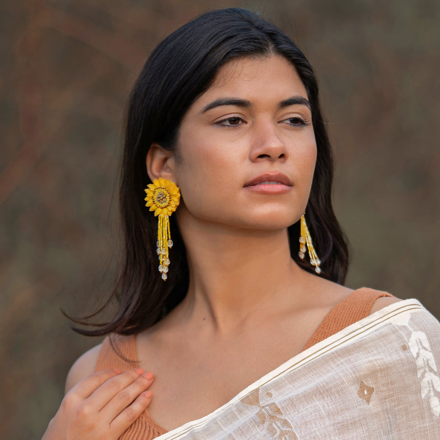 A model wearing the Sunflower Yellow DAHLIA Embroidered Earrings by Fyoli Fyoli, paired with a white and gold top. The handcrafted 3D flower and delicate beaded fringe add an elegant, nature-inspired touch to her look.